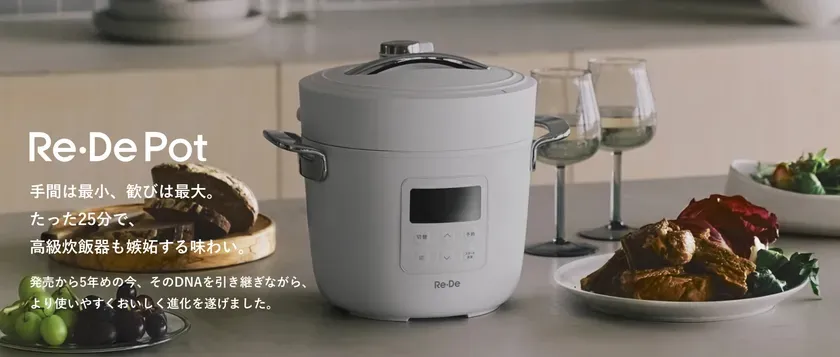 白を基調としたキッチンに置かれた、Re・De Potという電気調理鍋の画像。調理された料理、パン、ワイングラスなどが配置され、おしゃれな雰囲気を演出している。シンプルで洗練されたデザインが特徴的。