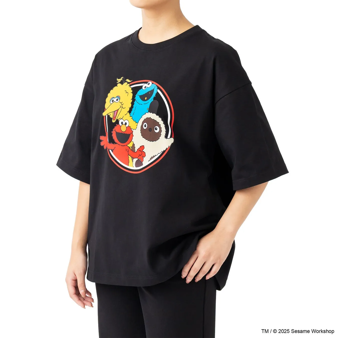 黒いTシャツを着た女性。Tシャツにはセサミストリートのキャラクターが描かれており、エルモ、クッキーモンスター、ビッグバード、そしてモッピーが描かれている。
