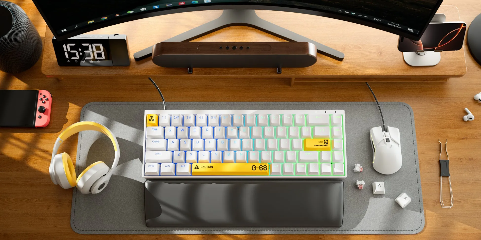 木製の机の上に、白いメカニカルキーボード、マウス、ヘッドホン、Nintendo Switch、目覚まし時計、スピーカー、イヤホン、スマートフォンホルダーなどのガジェットが配置された画像です。キーボードには、黄色いアクセントキーとG-68の文字が見えます。全体的に、モダンで洗練されたデスクセットアップを示しています。