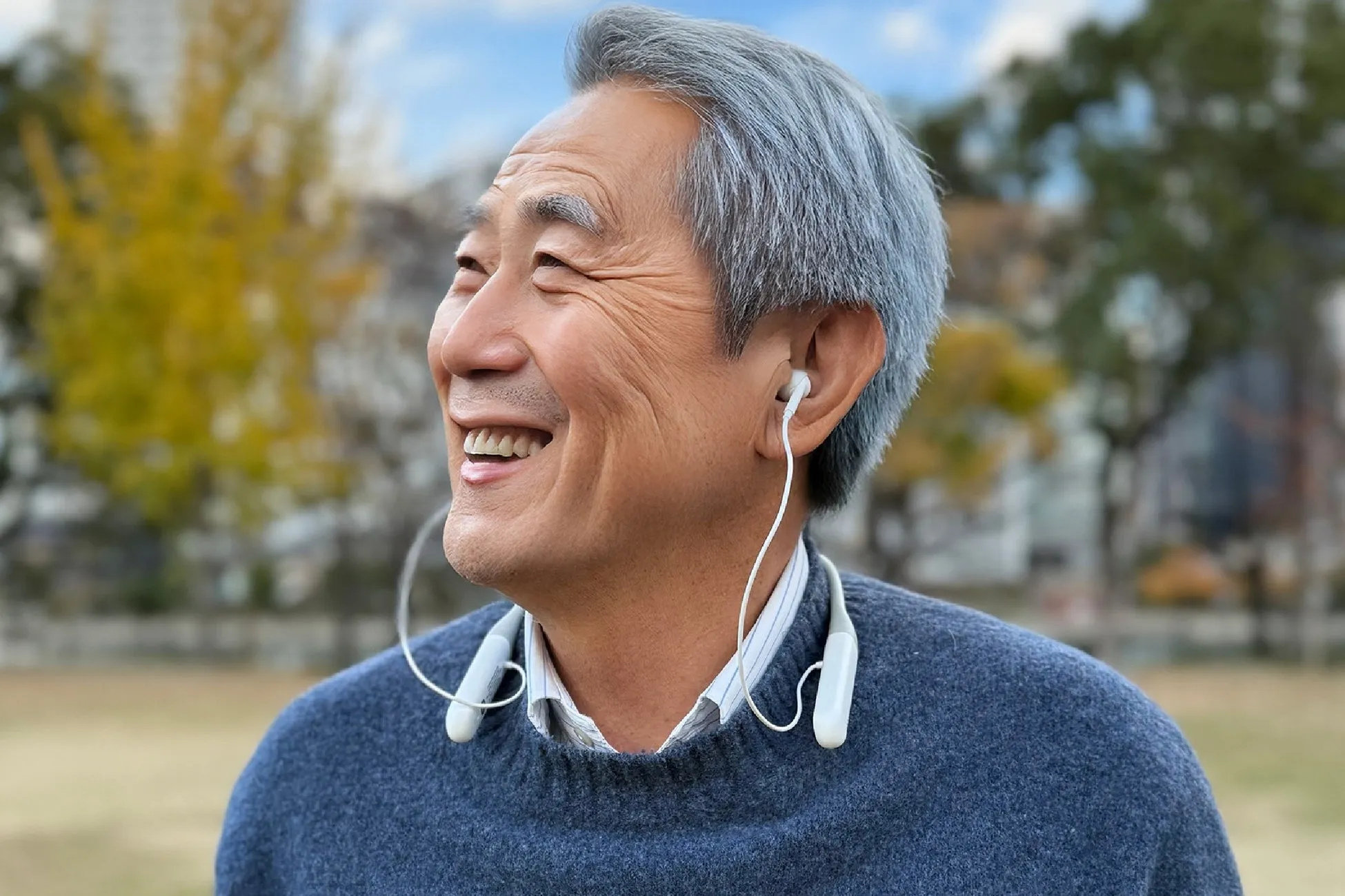 屋外で穏やかに微笑む高齢男性が白いイヤホンを装着しているアップ