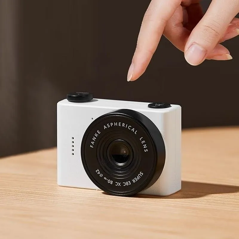 白い小型カメラと指のクローズアップ写真。カメラはテーブルの上に置かれており、レンズには「FANKE ASPHERICAL LENS」と書かれています。