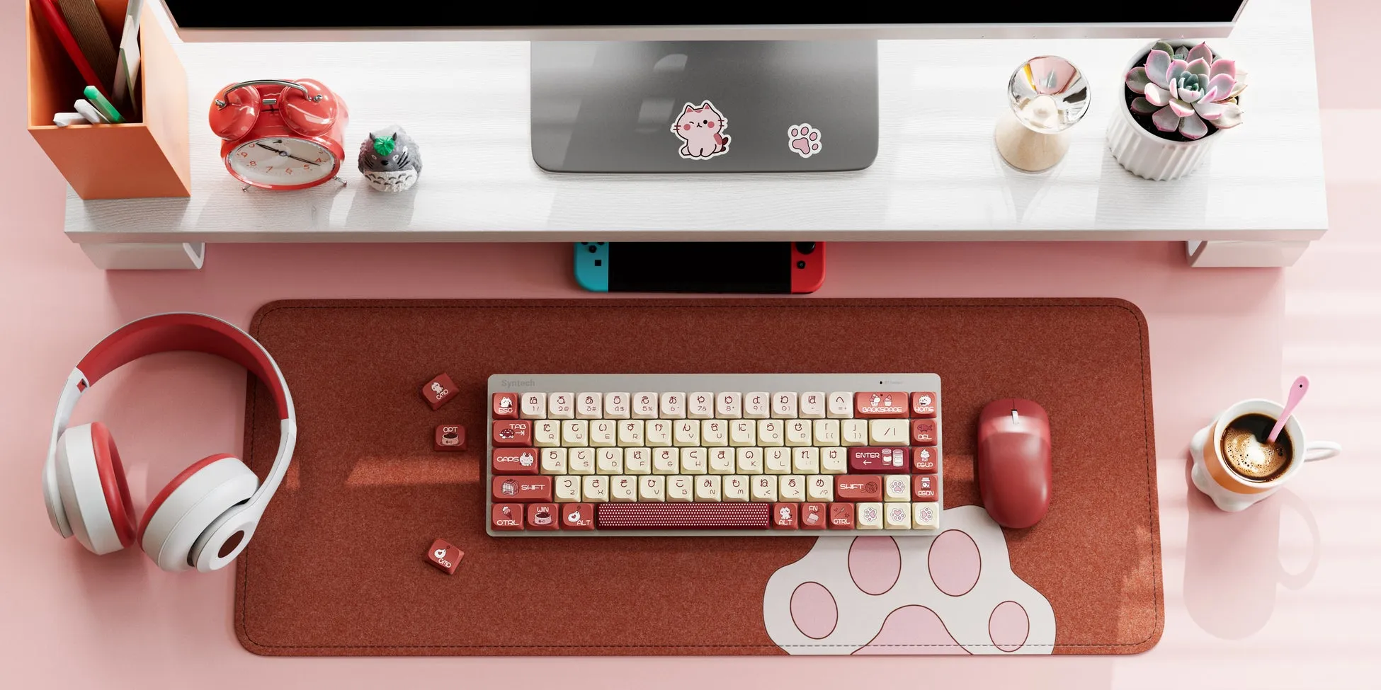ピンク色のデスク周り。キーボード、マウス、ヘッドホン、コーヒーカップ、目覚まし時計、多肉植物などが配置されている。